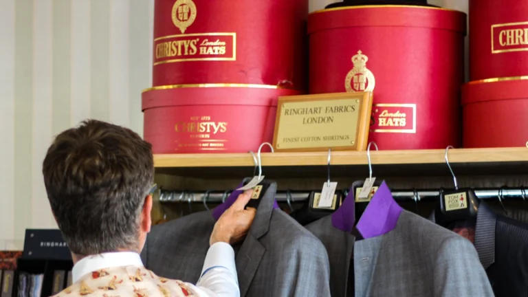 Philip Denning from Tom Fox Bespoke Tailoring holding a suit with red hat boxes on the shelf above.