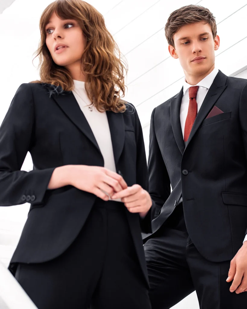 2 models wearing black sixth form suits. Female model with a white t-shirt and male model with a red tie.