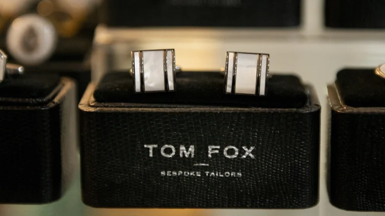 Square Mother of Pearl cufflinks in a Tom Fox Bespoke Tailors branded box, on a shelf.
